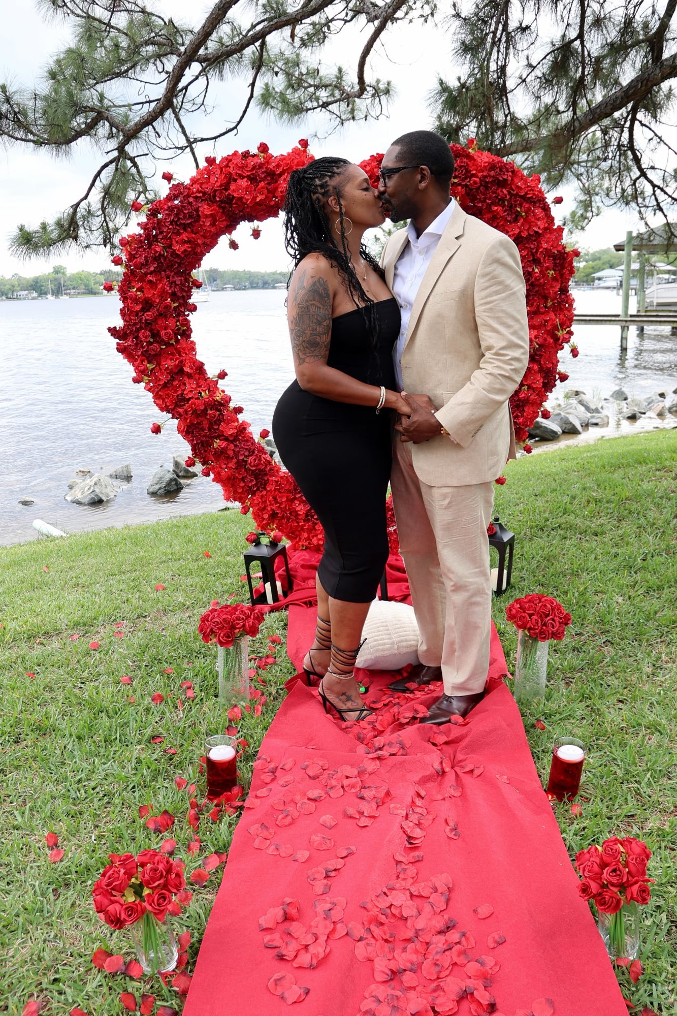 The couple kissing beneath the heart of roses at the water's edge.